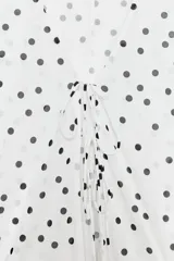 Top de crepe blanco con estampado de lunares negros, escote en V y cierre frontal con finas lazadas. Presenta mangas largas abullonadas con puños elásticos y bajo redondeado.