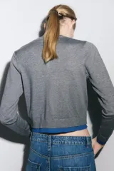 Chaqueta de punto gris de manga larga, cuello redondo y cierre frontal con botones oscuros. Presenta ribetes y detalles en color azul eléctrico en el frente, puños y ruedo.