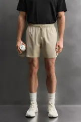 Pantalón corto deportivo color marrón oliva, confeccionado en tejido técnico ligero y elástico, con forro interior. Presenta cintura elástica ajustable con cordón, bolsillos frontales, bolsillo de seguridad trasero con cierre y aberturas laterales en el bajo.