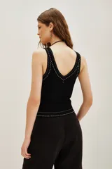Musculosa negra de tejido de punto, ajustada al cuerpo, con escote en V y detalles de pequeños apliques blancos (similares a tachas o puntos) bordeando el escote y la cintura.