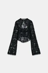 Top de encaje negro con cuello alto, mangas largas acampanadas, corsé interior estructurado y bajo asimétrico.