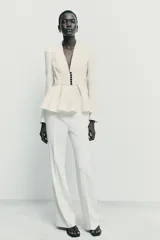 Blazer entallado de color crema con rayas verticales finas, cuello sin solapa y manga larga con hombreras. Presenta un diseño con bajo en evasé tipo peplum y cierre frontal con botones negros.