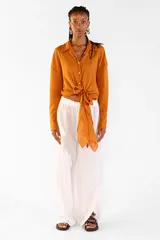 Camisa de algodón color tostado, de manga larga, con cuello camisero, botones frontales y detalle de lazo ajustable en la cintura.