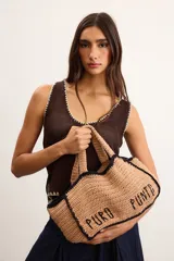 Bolso tipo tote mediano confeccionado en crochet artesanal color tostado, con detalles de bordes y costuras en contraste color negro. Presenta la inscripción "PURO PUNTO" bordada en el frente y asas dobles para llevar al hombro o en la mano.