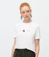 Remera de algodón color blanco, de corte clásico con cuello redondo y manga corta. Presenta un delicado bordado de tres pequeños íconos florales en el centro del pecho.