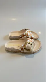 Sandalias planas de cuero color beige con diseño pintado a mano en tonos dorados, marrones y blancos, tira ancha con hebilla metálica grande y plantilla anatómica.