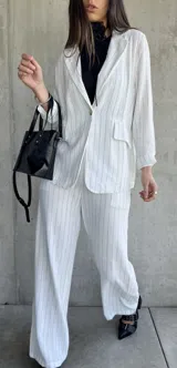 Blazer blanco con finas rayas verticales negras, solapas clásicas, cierre con un botón y bolsillos frontales.