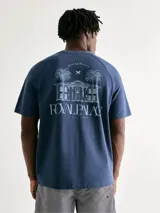 Camiseta azul de manga corta con cuello redondo y estampado frontal con palmeras y texto.