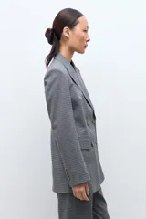 Blazer de corte sastre con doble botonadura frontal, solapas clásicas y bolsillos laterales con solapa. Presenta un diseño estructurado con estampado de microcuadros.