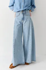 Pantalón de jean estilo wide leg con bordados pequeños de figuras deportivas. Presenta un diseño de tiro alto, corte holgado y ruedo desflecado.
