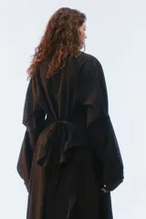 Camisa oversize negra de algodón liviano con textura calada, cuello camisero, botones frontales, mangas largas voluminosas y tiras para anudar en la espalda.