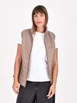 Chaleco acolchado de diseño matelasse, color beige, con cuello alto, cierre frontal y bolsillos laterales.