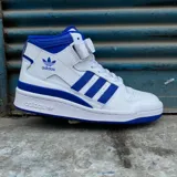 Zapatillas Adidas Forum Mid blancas con detalles en azul, con las tres tiras laterales en azul y ajuste con cordones y tira de velcro.