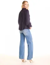 Blusa Tahari de gasa satén color violeta oscuro, con cuello alto fruncido y mangas largas abullonadas. La espalda tiene una abertura central con cierre de botón.