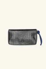 Billetera rectangular de cuero vacuno con textura de reptil, cierre perimetral y tirador de muñeca en color azul. Presenta un aplique metálico circular en el centro.
