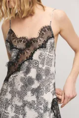 Top de satén con estampado estilo paisley en tonos blanco y negro, corte al bies, escote en V con apliques de encaje negro en el escote y el ruedo asimétrico. Cuenta con breteles regulables y tirantes finos.