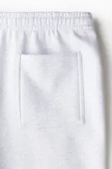 Pantalón deportivo de tejido de felpa color gris melange, con interior cepillado suave. Presenta cintura elástica con cordón de ajuste oculto, bolsillos laterales y un bolsillo trasero abierto. Las piernas terminan en puños acanalados.