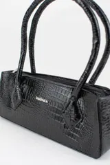 Cartera tipo baguette color negro con textura efecto cocodrilo, diseño alargado, doble asa de mano y cierre superior.