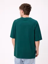 Remera de corte holgado color gris melange, con mangas raglán y estampado frontal con el logo de la marca Rusty en tonos azul y rojo.