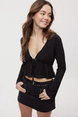 Blusa manga larga de color negro con escote en V profundo y lazo ajustable en el frente, confeccionada en tejido liviano con corte evasé.