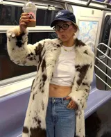 Tapado midi de piel sintética con estampado de manchas tipo vaca en tonos blanco y marrón. Presenta cuello amplio, cierre frontal con botones y corte recto de ajuste relajado.