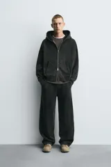 Sudadera con capucha y cierre de cremallera, de corte relajado (relaxed fit), confeccionada en algodón con interior afelpado. Presenta bolsillos frontales tipo canguro y acabados en rib. El tejido tiene un efecto lavado que le da un color negro desgastado.