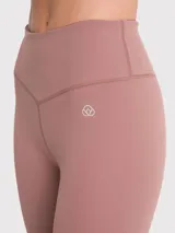 Calza deportiva de tiro alto con largo hasta el tobillo, confeccionada en tejido elástico de color rosado tierra. Presenta un diseño minimalista sin bolsillos y un pequeño logo bordado en la cadera.