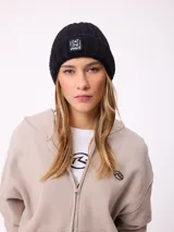 Gorro tipo beanie de punto acanalado en color negro, con parche frontal rectangular que incluye la frase 'Eat the wave' bordada en blanco.