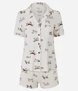 Pijama de dos piezas confeccionado en viscolycra con estampa de perros de color marrón sobre base blanca. Incluye una camisa de manga corta con solapas, cierre frontal con botones y un bolsillo en el pecho, y un short a juego con cintura elástica.