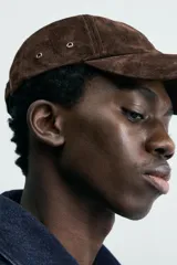 Gorra de béisbol color marrón oscuro, confeccionada en material con textura de ante o nobuk. Presenta visera curva y ojales metálicos a los lados para ventilación.