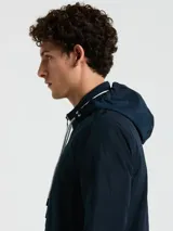 Campera rompevientos azul marino con cierre frontal, cuello alto con doble raya blanca, capucha oculta, puños elásticos y bolsillos con cierre.