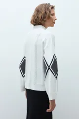 Media polera de tejido de punto color crudo, con diseño de rombos en el frente en tonos gris y negro. Presenta cuello alto y mangas largas.