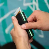 Billetera tipo tarjetero de cuero negro con caja de aluminio interna y sistema de deslizamiento para tarjetas. Cuenta con cierre mediante broche a presión.