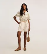 Short recto de cintura alta color crudo, confeccionado en viscolino, con trabillas en la cintura, pliegues y cierre tradicional. Incluye cinturón de rafia artificial con hebillas de argollas.