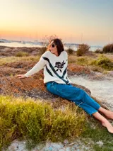 Sweater de lana color crema con cuello redondo, mangas largas y diseño con apliques de cuero negro en forma de V en el frente y bordado de una rosa negra en el pecho.