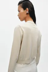 Chaqueta de punto efecto doble capa color beige, con cuello redondo, manga larga y cierre frontal con botones. Cuenta con un bolsillo de plastrón en el pecho y bajo acabado en rib.