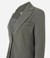 Blazer de sastrería color verde oliva, con corte oversized, solapas clásicas, cierre frontal de un botón y bolsillos con tapa. Cuenta con forro interno y textura sutil.