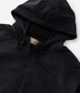 Campera rompeviento deportiva de color negro, con cierre frontal de cremallera, capucha ajustable con cordón, bolsillos laterales y ruedo elástico. Presenta recortes delanteros y diseño de manga larga.
