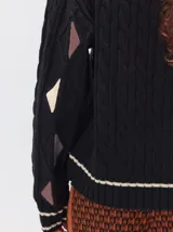 Sweater de tejido de punto trenzado en color marrón, con cuello redondo, puños y ruedo acanalados. Presenta detalles de franjas en color naranja en el cuello y el ruedo, además de apliques de rombos en tonos naranja y verde en las mangas.