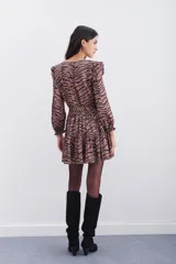 Vestido corto con estampado de cebra en tonos marrón y negro. Presenta mangas largas con puños elásticos, volados en los hombros y cintura elástica con lazo ajustable. Tiene tachas metálicas termo adhesivas en el escote y hombros.