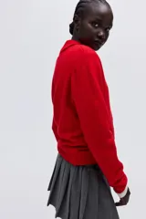 Cárdigan de punto suave color rojo, con cuello redondo ribeteado y cierre frontal de botones oscuros. Presenta puños y bajo acanalados.