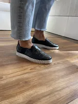 Zapatillas de cuero negro con diseño entretejido y suela blanca.