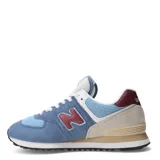 Championes New Balance modelo 574, color azul claro con gamuza azul más oscura, detalles en beige claro, rojo oscuro en el talón y logo 'N' en rojo oscuro con borde blanco.