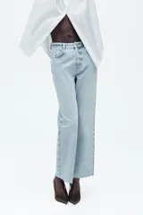 Jeans de tiro alto, corte recto y largo al tobillo, color blanco roto o crema. Presenta costuras contrastantes en tono claro y acabado sin dobladillo en el ruedo.