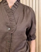 Camisa de denim de algodón celeste, con cierre frontal de botones, cuello alto con volados y mangas cortas abullonadas con puños elastizados fruncidos.