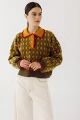 Buzo de punto con diseño de rombos en tonos mostaza y verde oliva. Presenta cuello polo con cierre frontal de tres botones, mangas largas con puños acanalados y detalles en color rojo en cuello, puños y ruedo.