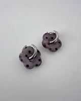 Aros de acero quirúrgico con argolla plateada y dije de flor translúcida en color lila con lunares negros.