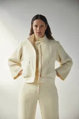Campera de lana fina color crema, con cuerpo estructurado y mangas de tejido de punto acanalado. Presenta cuello alto, cierre frontal con botones y bolsillos laterales con doble abertura.