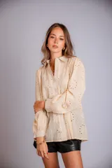 Camisa de manga larga en color beige, confeccionada en tela con bordado inglés y diseño de flores caladas. Presenta cuello clásico, cierre frontal con botones y puños abotonados.