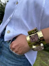 Brazalete rígido de bronce con diseño ancho y acabado pulido, decorado con piedras naturales de textura rugosa engarzadas en el metal.
